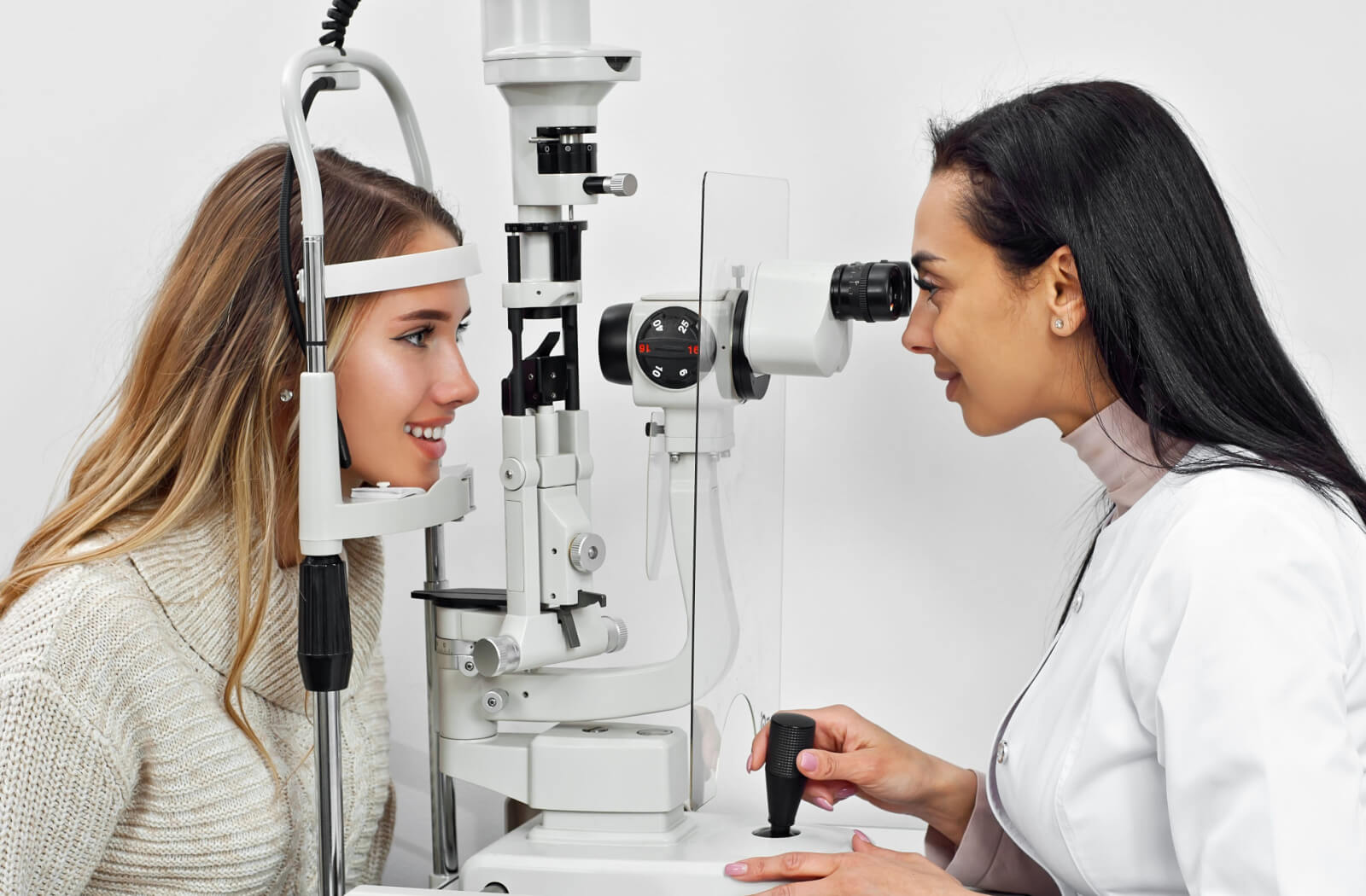 A female optometrist using a medical device to examine the eyes of a female patient and look for potential eye problems.
