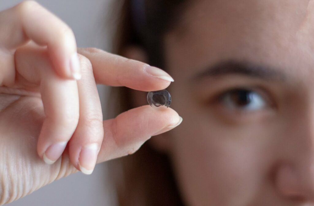 An Ortho-K contact lens being held by a woman between her index finger and thumb.