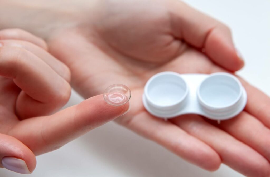 A person holding a white contact lens case with a single contact lens on the tip of their index finger