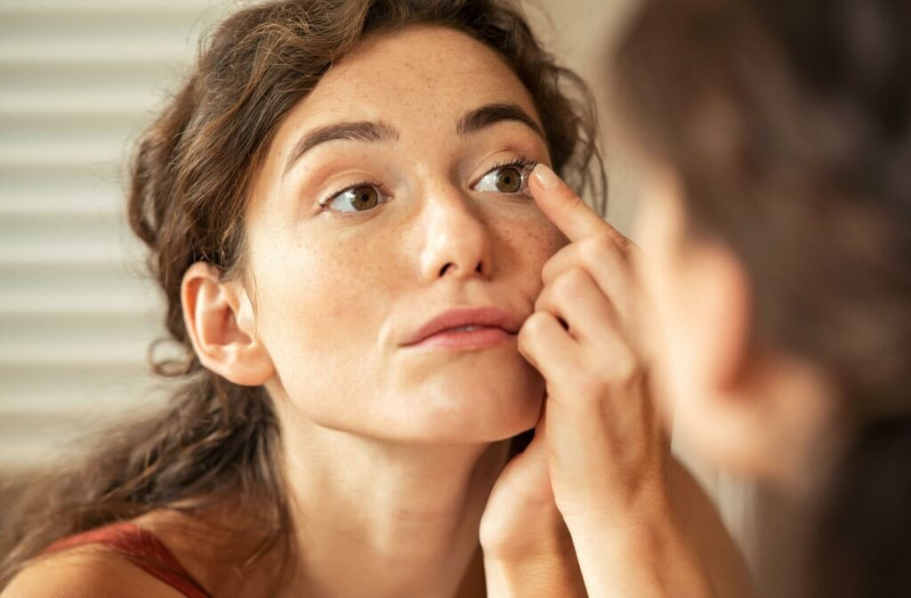 A young woman focusing in the mirror as she inserts her contact lens.