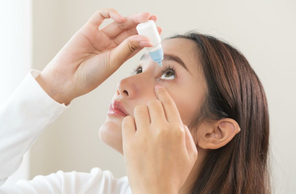 A young adult carefully inserting eye drops into their left eye to reduce their dry eye discomfort.