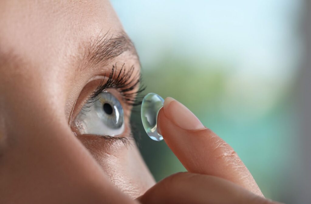 A close-up image of a young adult carefully inserting a large scleral lens into their left eye to help with dry eye discomfort.
