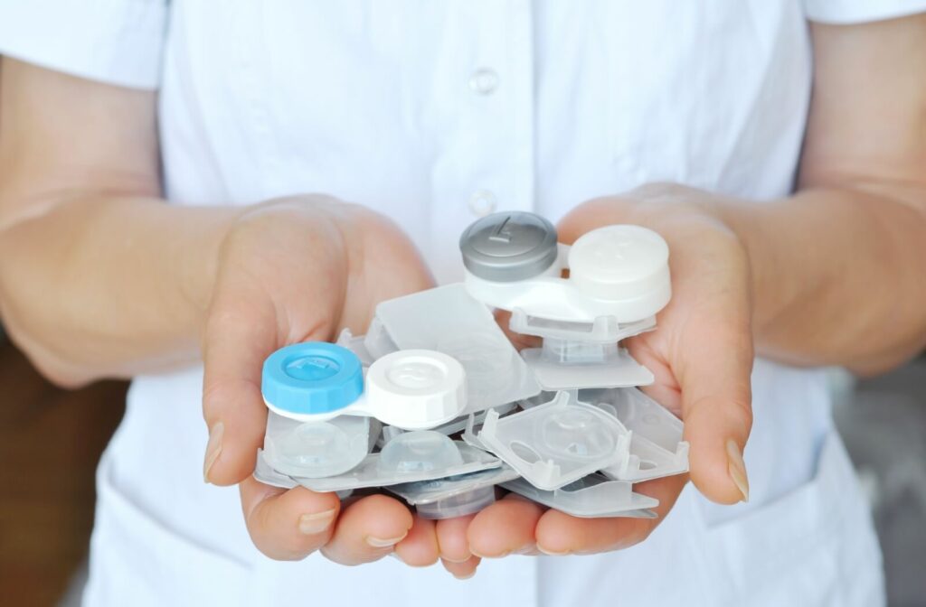 A close-up image of a person holding several blister packs with contact lenses and two contact lens cases in their hands.