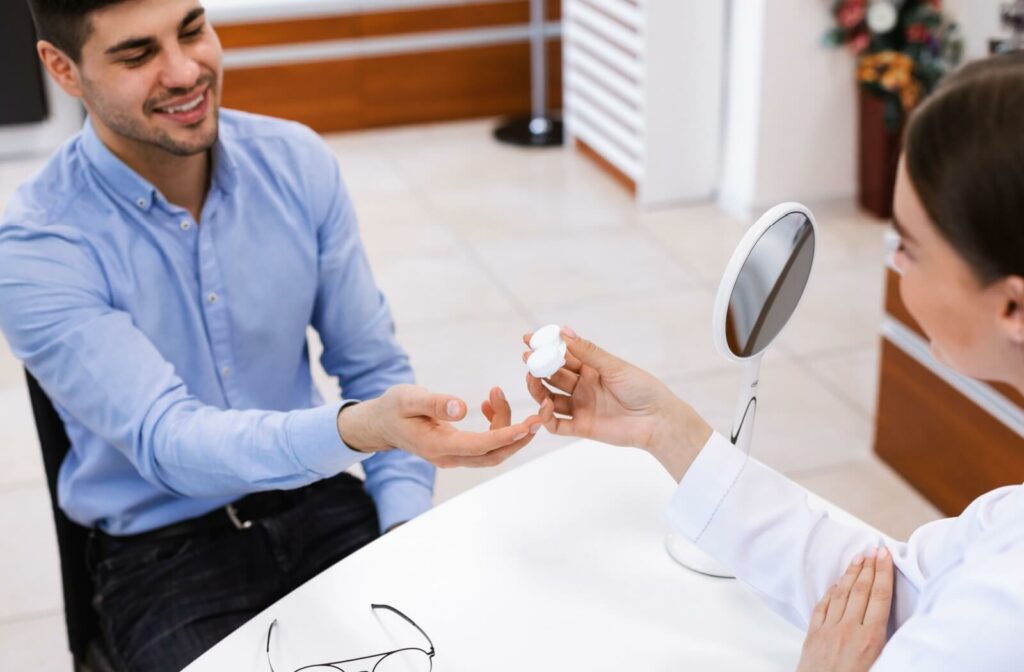 An eye doctor showing a smiling customer a contact lens container with contacts during a consultation.
