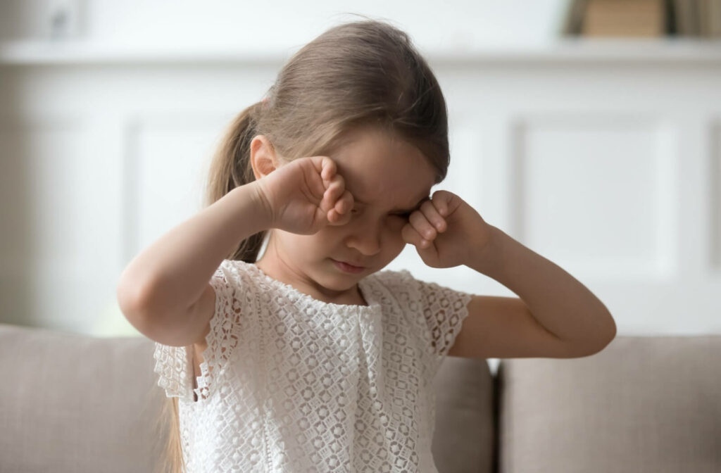 A child rubbing their eyes with both hands from a vision problem.