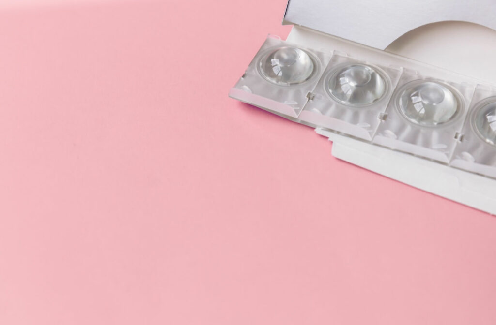 An opened supply of daily disposable contacts resting against a pink background.