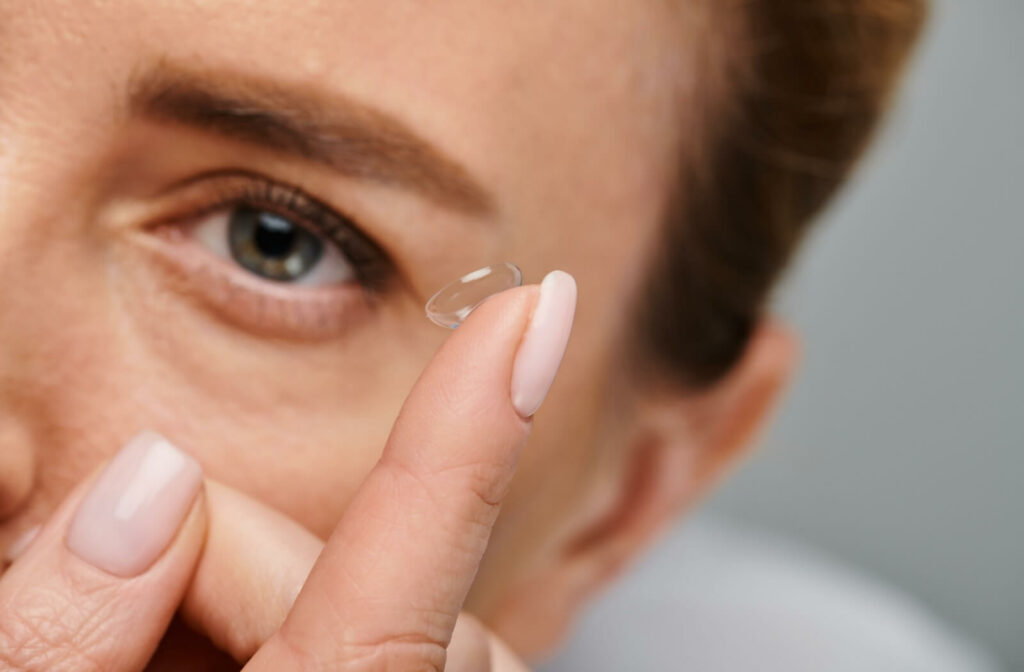 A woman holding a clear contact lens on her fingertip preparing to insert it with care