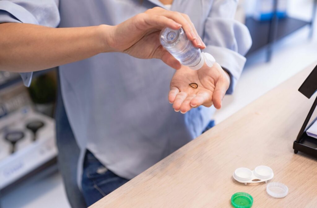 A person cleaning a contact lens with fresh solution over their hand next to a contact lens case