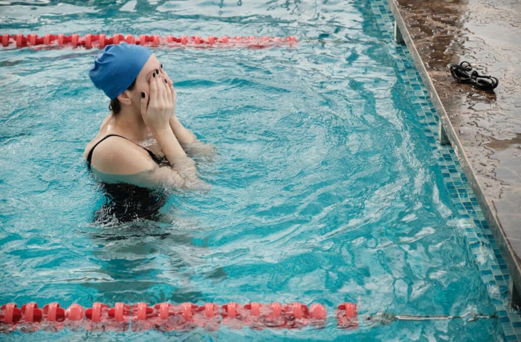 A person rubbing their irritated eyes from wearing contact lenses in a lane swimming pool.