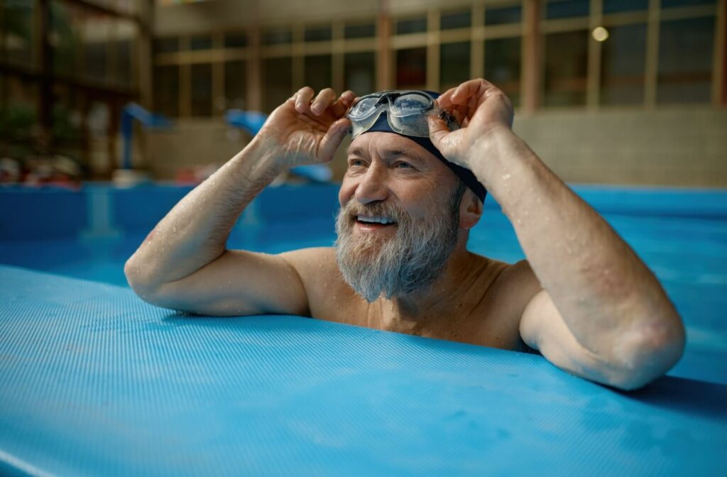 A swimmer standing at the edge of a pool, preparing to put on goggles to protect their contact lenses from water.