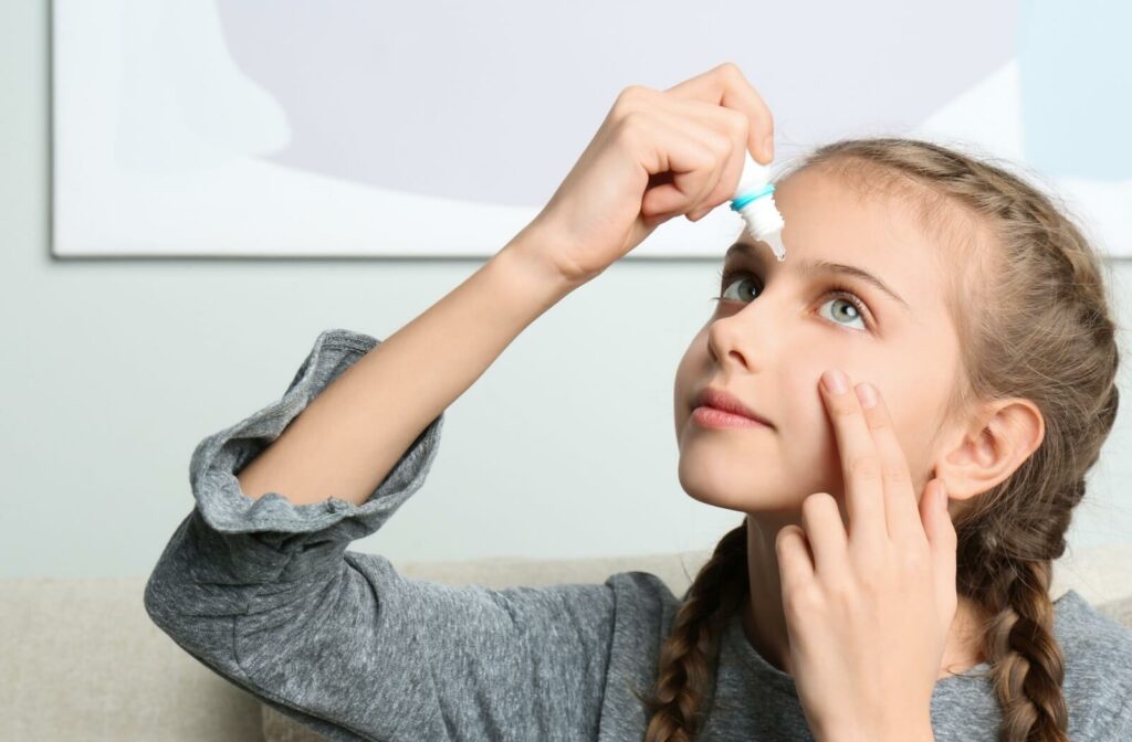 A young child carefully applying eye drops to their left eye.