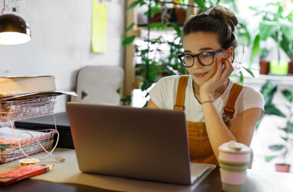 A smiling adult uses their computer comfortably with properly fitting glasses with the right prescription.